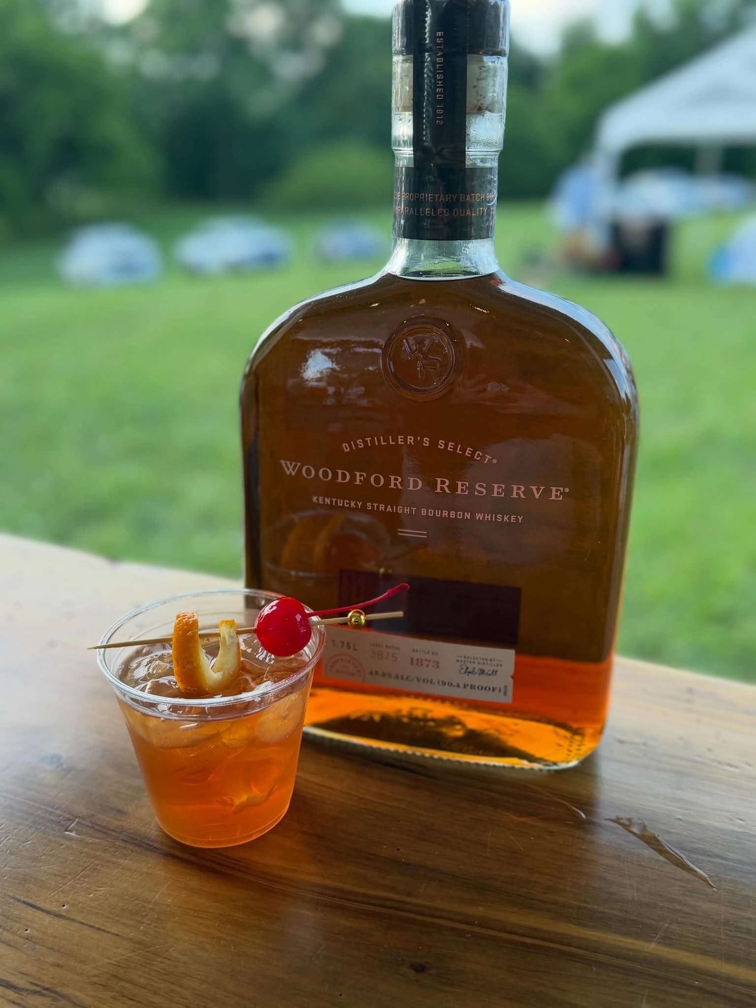 Old fashioned with an orange twist and cherry, beside a bottle of Woodford Reserve