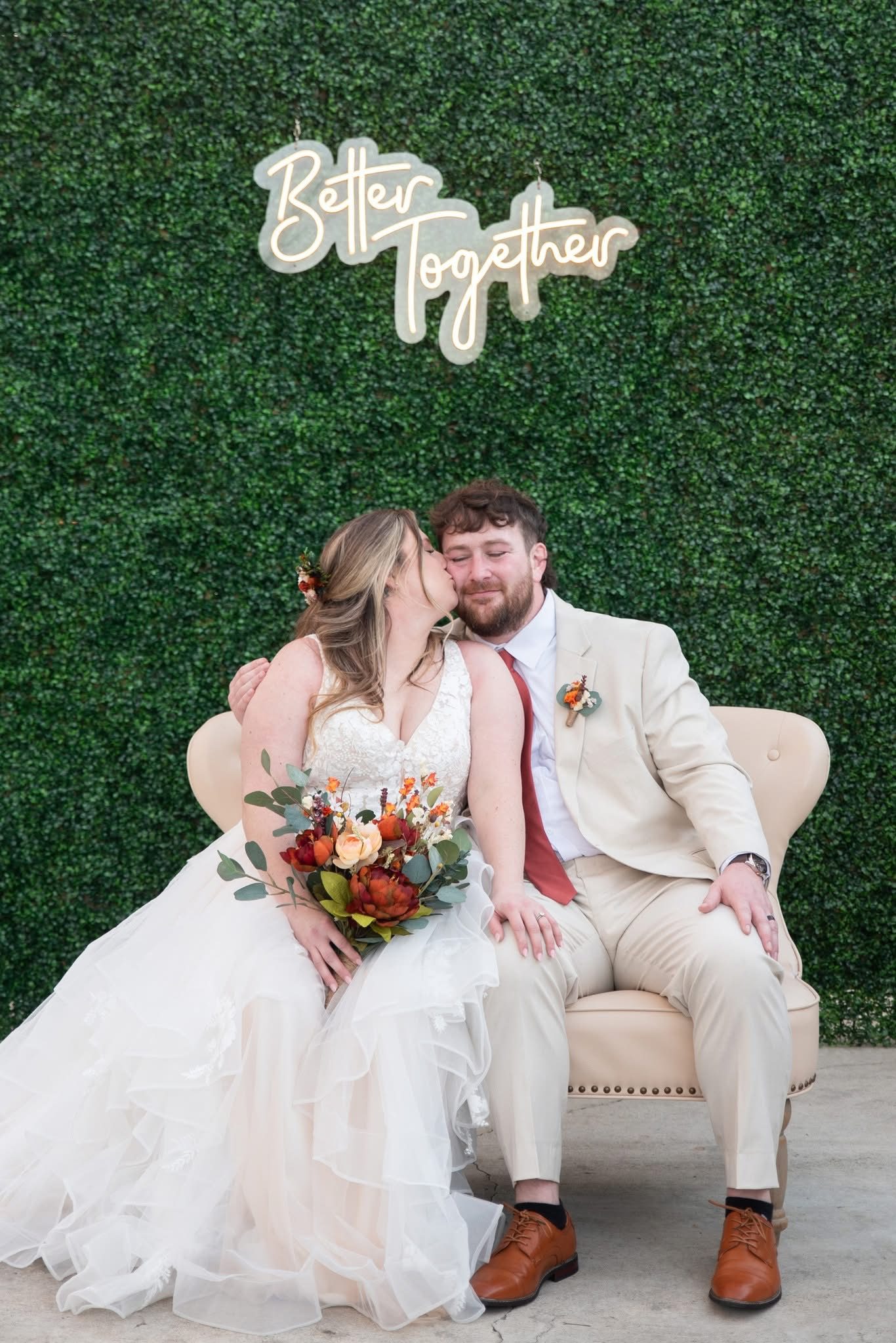 Bride and groom on a vintage sofa beneath a Better Together neon sign